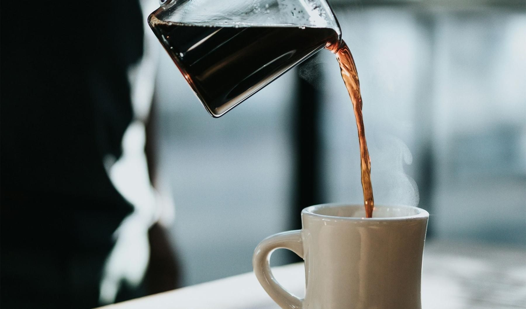 a person pouring a carafe of coffee into a cup